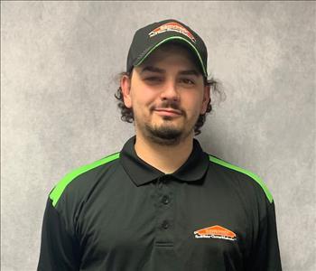 employee posing in a black cap and SERVPRO logo hoodie